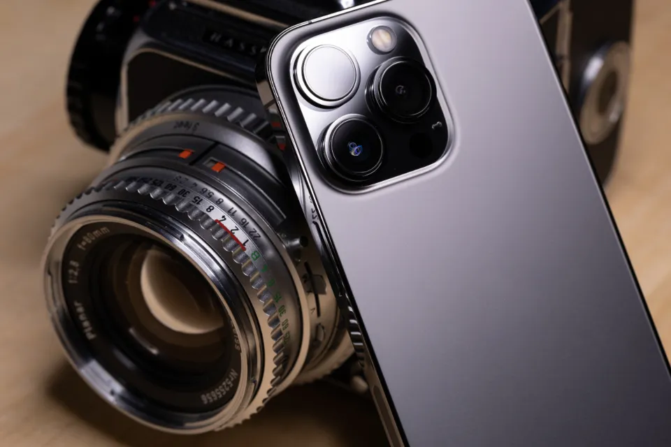 The camera lenses of a smartphone leaning against an old film camera