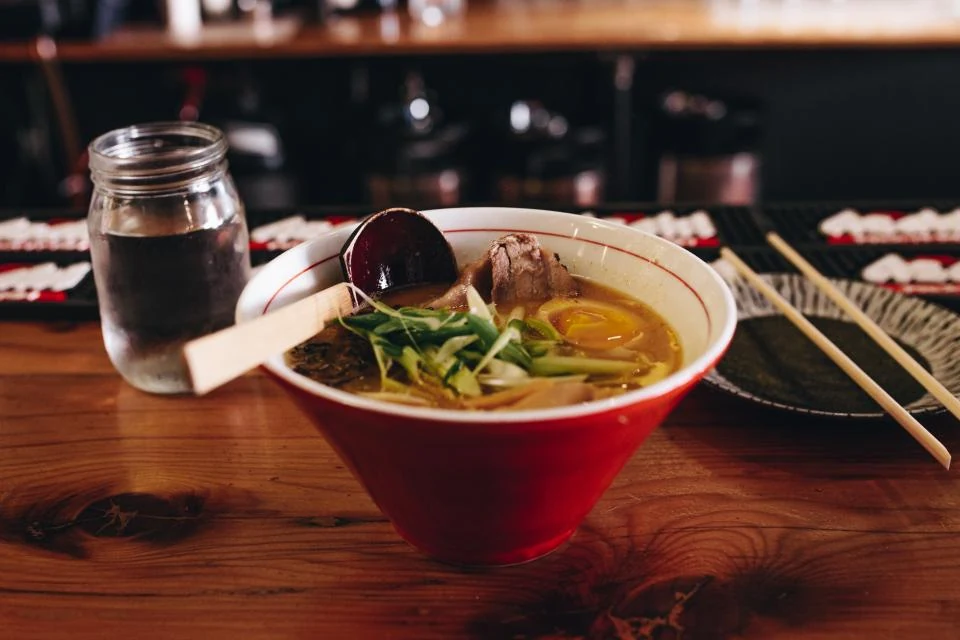 Rote Schale mit Nudelsuppe, Ei und Frühlingszwiebeln auf einem Holztisch