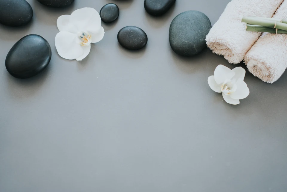Rolled towels, dark stones and white orchids on a grey table